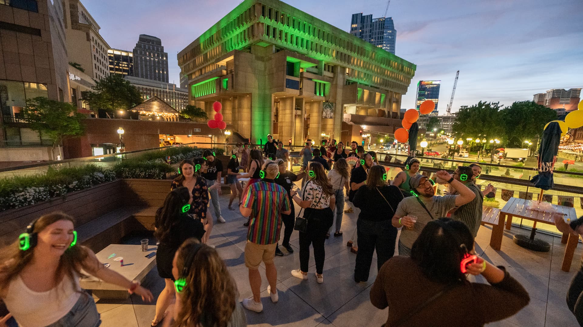 Silent disco crowd in glowing green headphones at dusk in downtown Boston