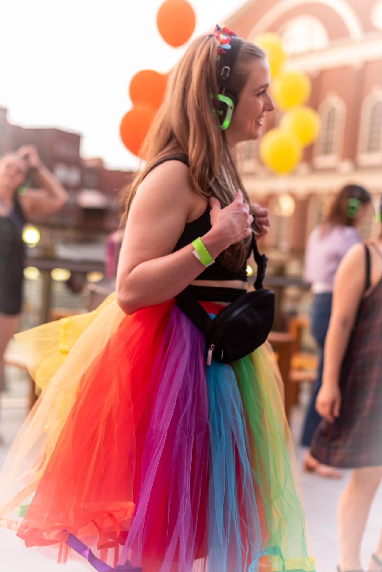 Guest in a rainbow tulle skirt and green silent disco headphones at a Pride party